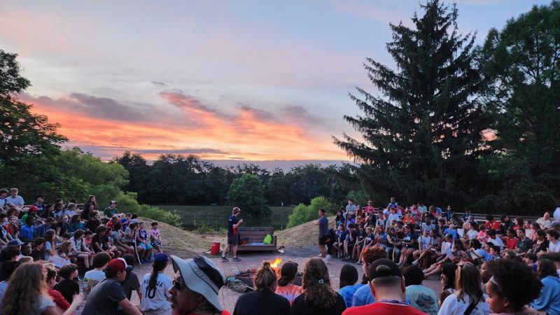 4-h summer camp, campfire circle, campers sitting around a campfire with a sunset in the background